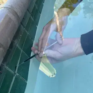 Pool technician performing dye testing along the tile line to pinpoint a hairline leak