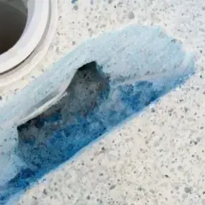 Crack in pool plaster near the skimmer being sealed with blue epoxy during a pool leak repair