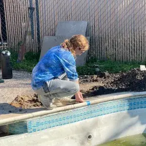 Female leak detection technician performing a dye test along the pool tile waterline to locate the leak