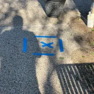 Blue spray-painted X marking the precise location of an underground water leak on a concrete patio